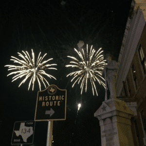 white fireworks above a statue and street signs